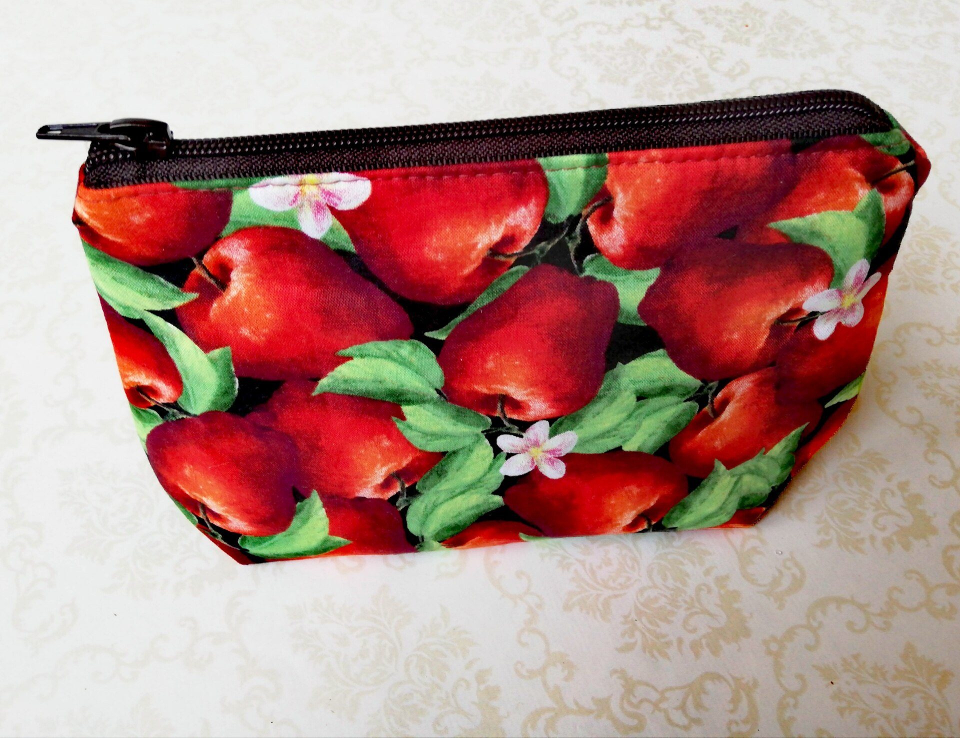 A zipped fabric pouch with a red apple print